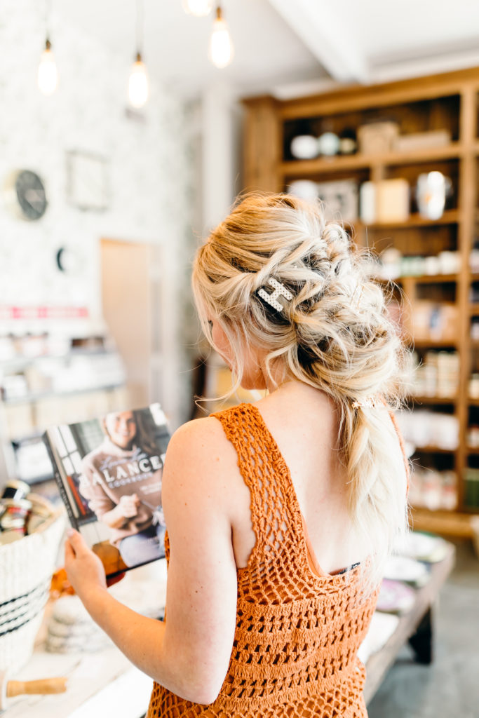 How to Wear Hair Clips by popular Nashville fashion blog, Nashville Wifestyles: image of a woman with a braided hairstyle and wearing a pearl letter H hair clip, gold bobby pins, and a star hair clip in her hair along with an orange crocheted maxi dress with fringe.