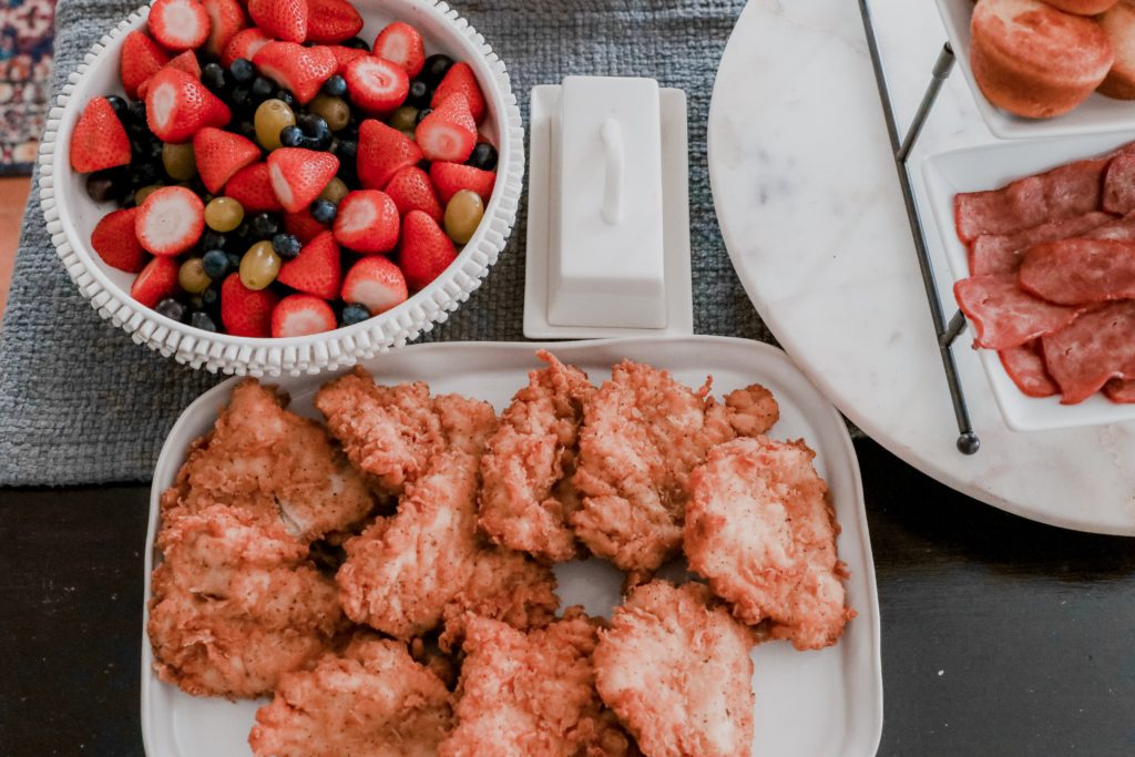 Southern Style Brunch Ideas That Pulls Out All the Stops - Nashville Wifestyles; I had family in town last weekend so I decided to throw a brunch together for my family and friends before watching college football that Saturday. There's nothing more tasty than a family weekend brunch made up of tasty brunch recipes. Click to read how to throw a Sunday brunch at home on Nashville Wifestyles! For the waffles, I used the Kodiak protein waffle mix. We also had turkey bacon, fresh cut fruit salad, Nashville fried chicken and more for our brunch meal. | Southern Style Brunch Ideas That Pulls Out All the Stops by popular Nashville lifestyle blog, Nashville Wifestyles: image of a bowl full of fruit, a platter of fried chicken, and a platter of bacon and biscuits. 
