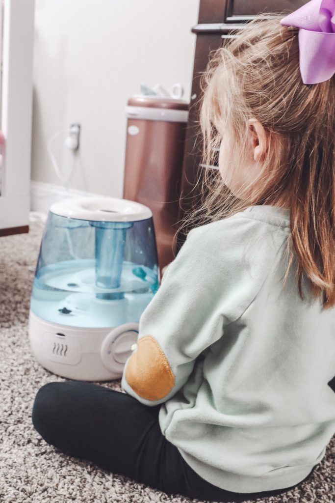 Soothe Coughs & Sore Throats with Vick's Filter Free Cool Mist Humidifier by popular Nashville life and style blog, Nashville Wifestyles: image of a little girl sitting next to a Vick's filter free cool mist humidifier.
