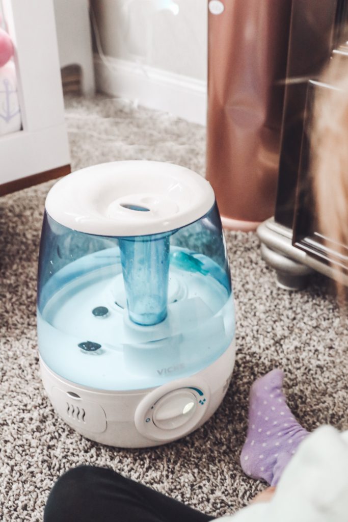 Soothe Coughs & Sore Throats with Vick's Filter Free Cool Mist Humidifier by popular Nashville life and style blog, Nashville Wifestyles: image of a little girl sitting next to a Vick's filter free cool mist humidifier.