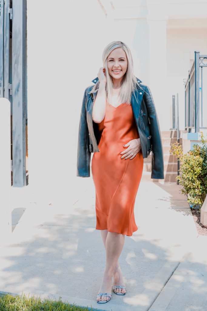 Edgy Date Night Look by popular Nashville mom fashion blog, Nashville Wifestyles: image of a woman wearing a leather jacket, rust colored satin midi dress, and heel sandals. 