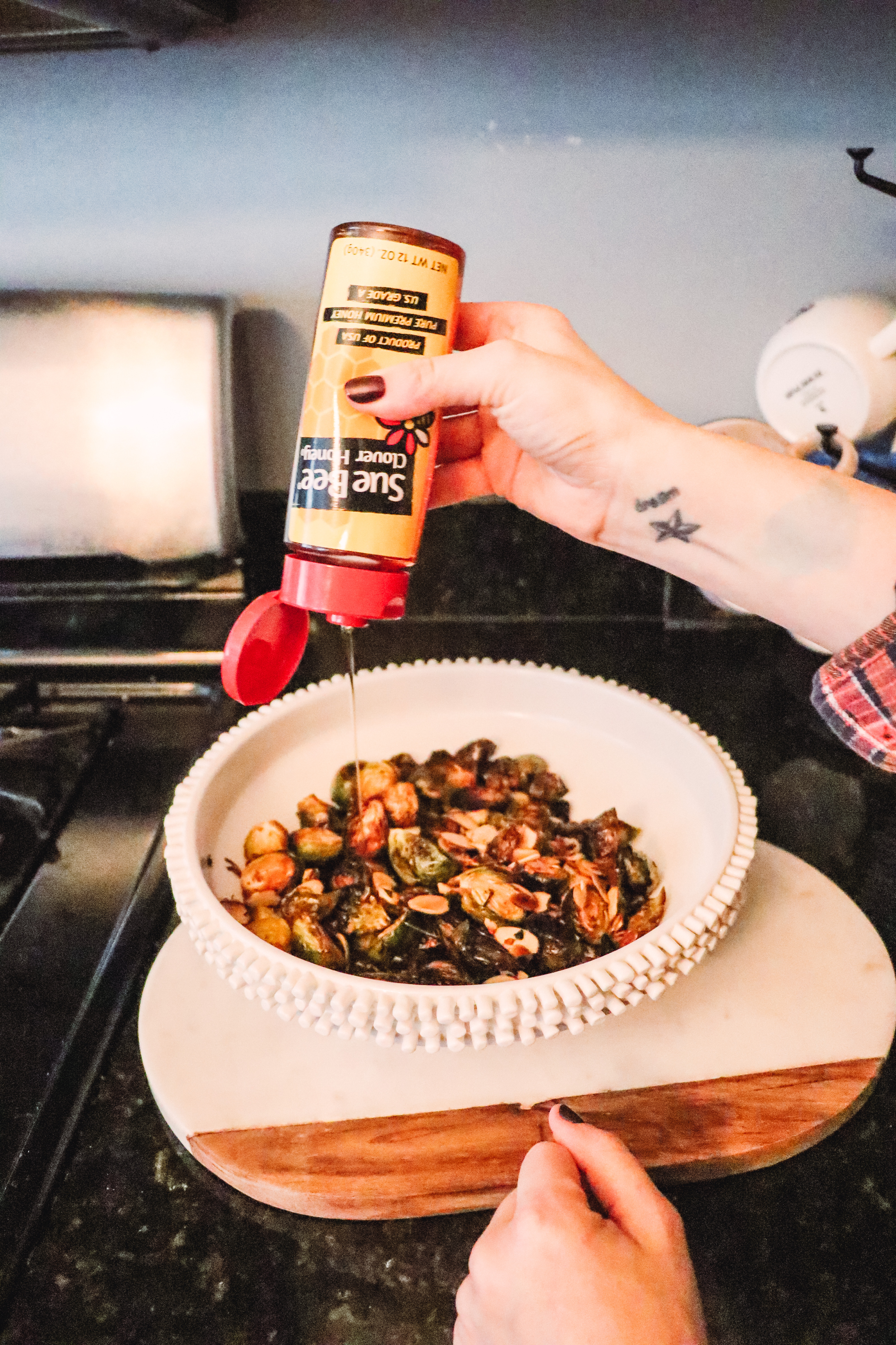 Honey Roasted Brussel Sprouts by popular Nashville life and style blog, Nashville Wifestyles: image of a woman drizzling Sue Bee honey on roasted Brussel sprouts.