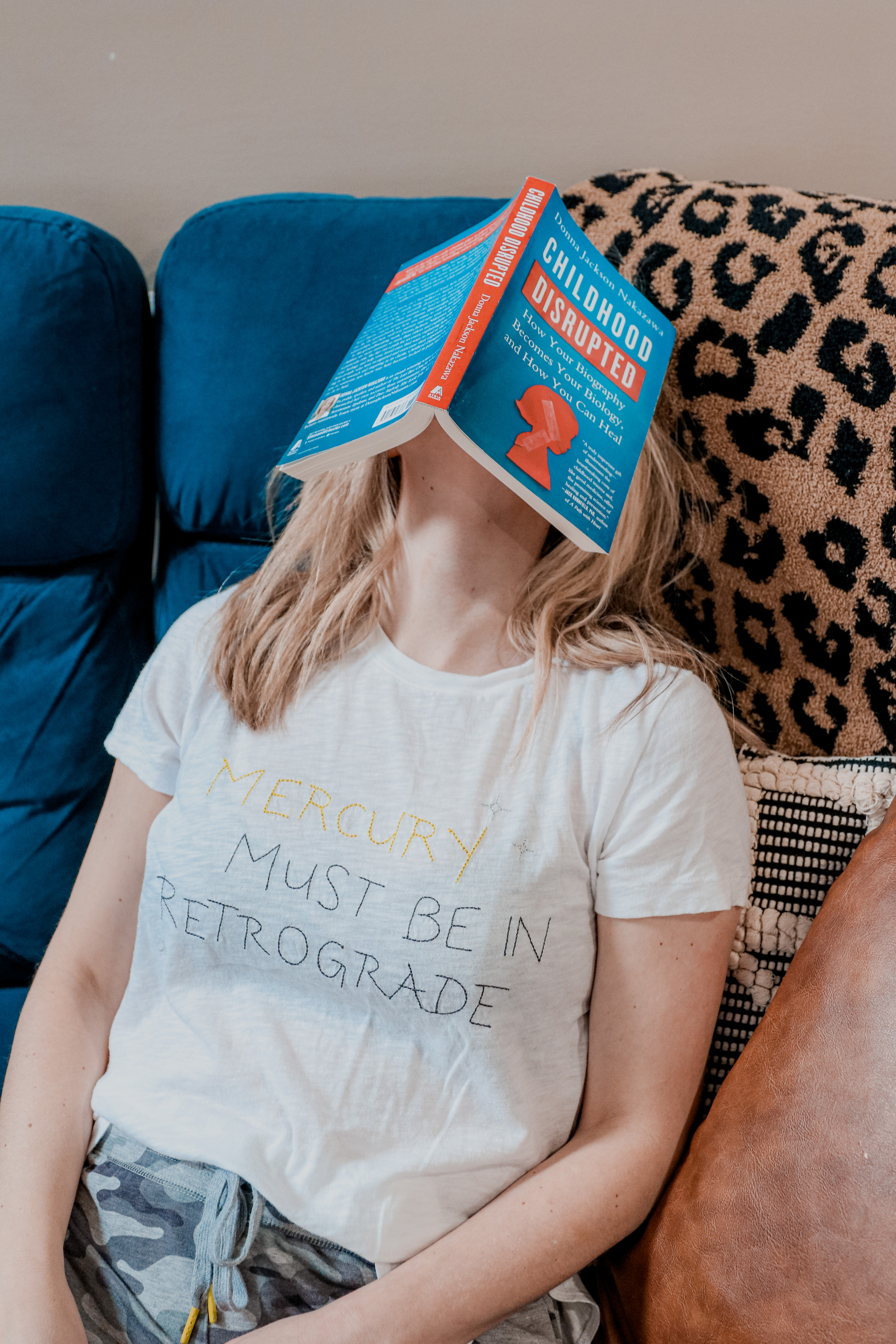 Self Healing Books by popular Nashville lifestyle blog, Nashville Wifestyles: image of a woman sitting on her blue couch and holding the Childhood Disrupted book.