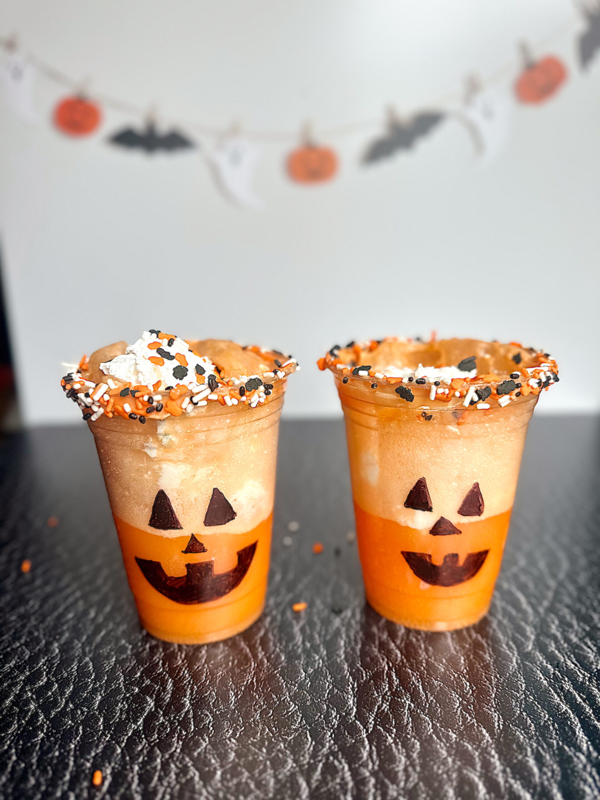 Jack-O’-Lantern Ice Cream Float in a clear cup with Halloween sprinkles and whipped cream on top.