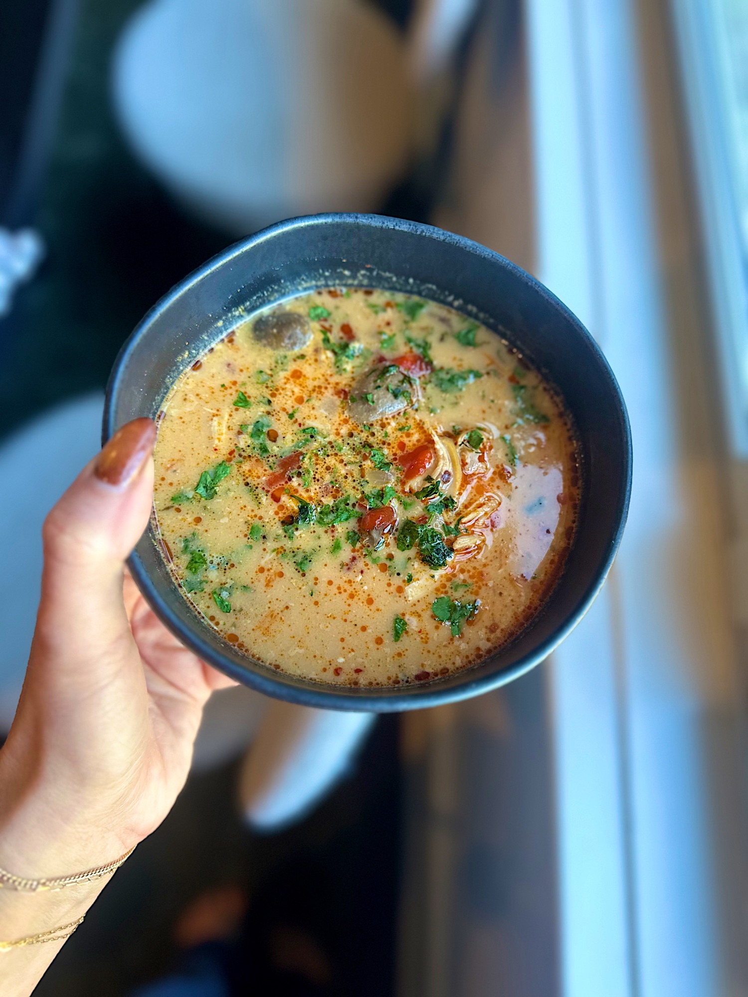 Bowl of red curry chicken soup topped with cilantro and sriracha